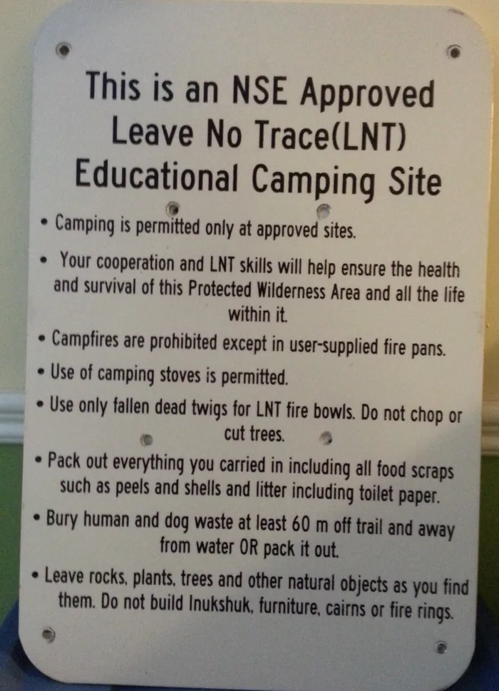 The white NSE Approved Leave No Trace Educational Camping Site sign, listing the rules for camping, fires, waste and natural objects.